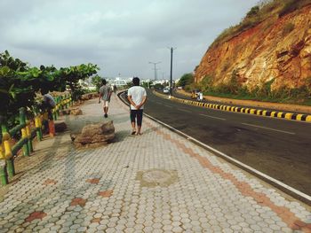 Rear view of man walking on road against sky