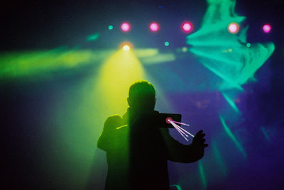 Rear view of man with arms raised at music concert