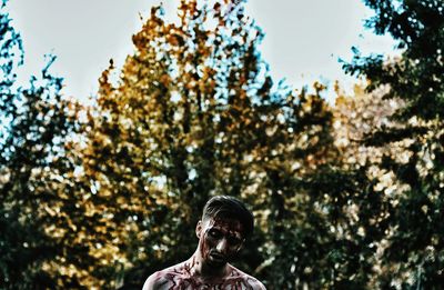 Low angle view of man covered in blood against trees