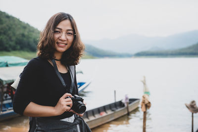 Portrait of beautiful young woman standing against lake