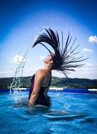 Man splashing water in swimming pool against blue sky