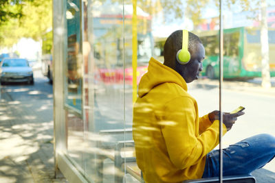 Man listening music while sitting at bus stop