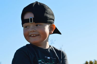 Close-up of smiling boy wearing cap against clear sky