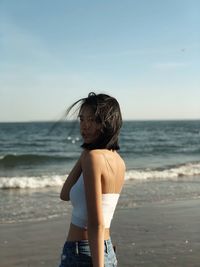 Rear view of boy standing on beach against sky