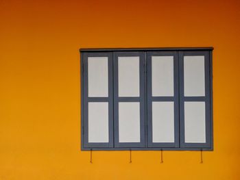 Close-up of yellow window on orange wall