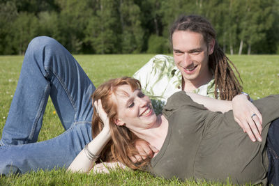 Portrait of happy man with pregnant woman relaxing on grassy field