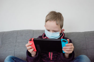 Boy playing with a game console with a face mask on as protection