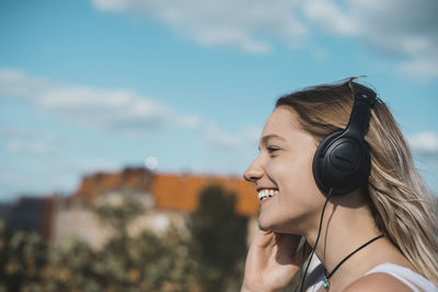 Smiling young woman listening to music against sky