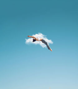 Full body side view of faceless sporty female acrobat doing somersault stunt on blue sky with cloud on summer day