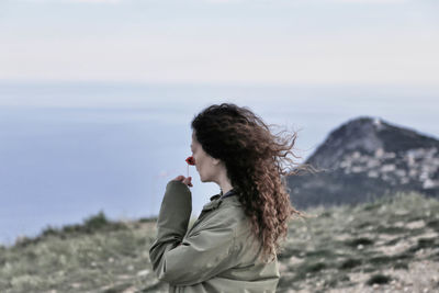 Side view of woman smelling flower against sky