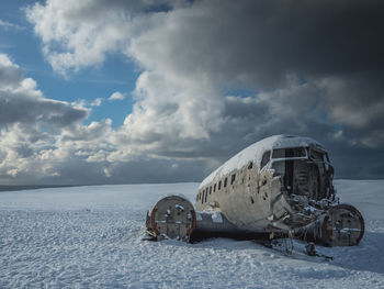 Abandoned airplane on snowy field against sky