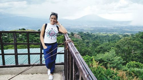 Portrait of smiling woman standing at railing against landscape