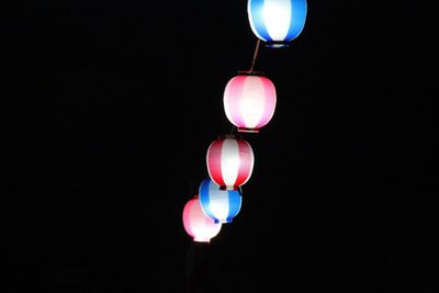 Low angle view of illuminated lanterns hanging over black background