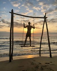 Silhouette man swinging against sea during sunset