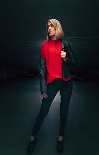 Portrait of young woman standing against black background