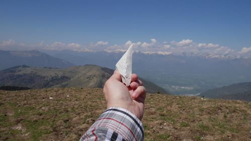 Cropped image of hand holding stone against cloudy sky