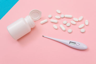White pills or tablets scattered from the pill container with electronic thermometer