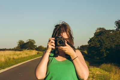 Portrait of woman photographing on field against sky