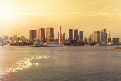 Sea by buildings against sky during sunset