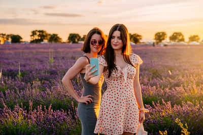 Full length of woman with arms raised on field against sky during sunset