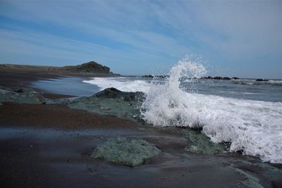 Waves splashing on rocks at shore against sky in island