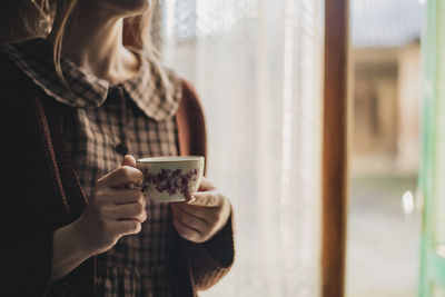 Midsection of woman holding coffee cup by window