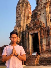 Portrait of young man in prayer position standing against temple