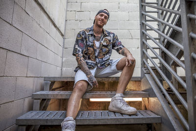 Young man sitting on staircase against wall