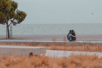 People sitting on land by sea against sky