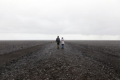 Rear view of couple walking on dirt road amidst landscape