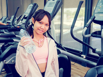 Portrait of smiling girl holding water bottle while standing gym