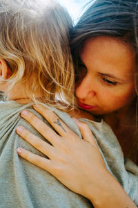 Positive mother embracing adorable little kid having fun and laughing together in woods during summer weekend