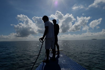 Rear view of men standing by sea against sky