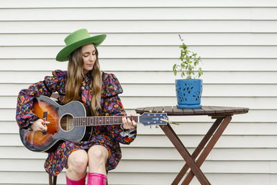 A beautiful woman sits at an outdoor table playing an acoustic guitar