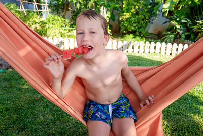 Portrait of shirtless eating watermelon sitting on hammock