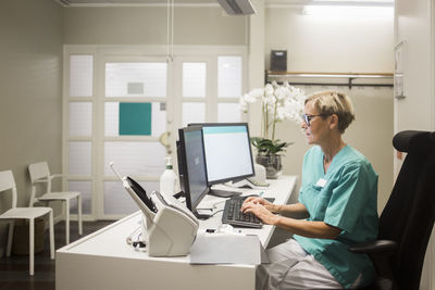 Side view of mature female doctor working over computer while sitting in clinic