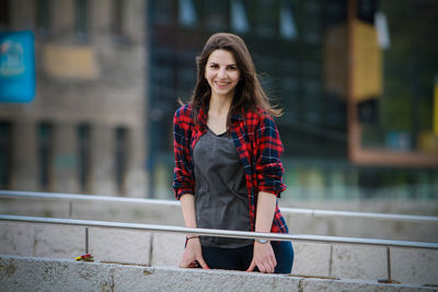 Portrait of smiling young woman standing against railing