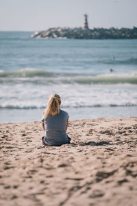 Rear view of woman sitting at beach against sky