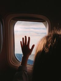 Rear view of girl looking through window while traveling in airplane