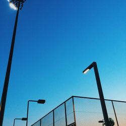 Low angle view of street lights by chainlink fence against clear sky