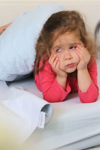 Bored girl with hands on chin lying at bed