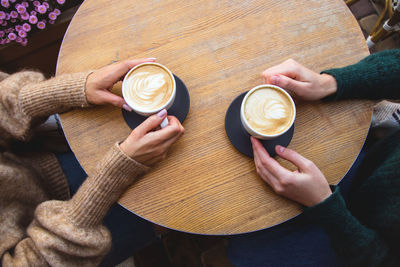 Midsection of women holding coffee cups on table