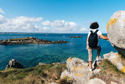 Rear view of woman standing on cliff by sea