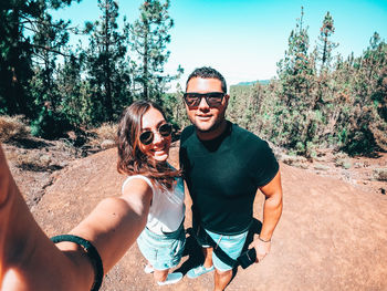 Portrait of smiling couple wearing sunglasses doing selfie against forest