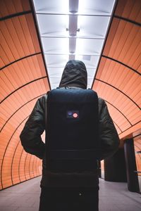 Rear view of man wearing backpack walking in illuminated subway tunnel