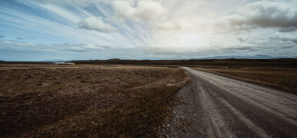 Dirt road on field against sky