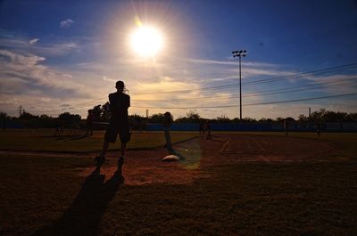 Silhouette players playing baseball on field against sky during sunset