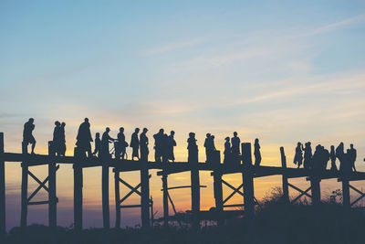 Silhouette people standing by railing against sky during sunset