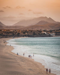 People at beach against sky during sunset