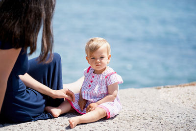 Midsection of mother with daughter sitting against sea